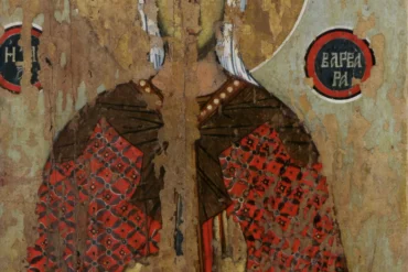 Saint Barbara stands against golden light in 14th century Byzantine icon, wearing rich robes and holding martyr's cross in prayer gesture.